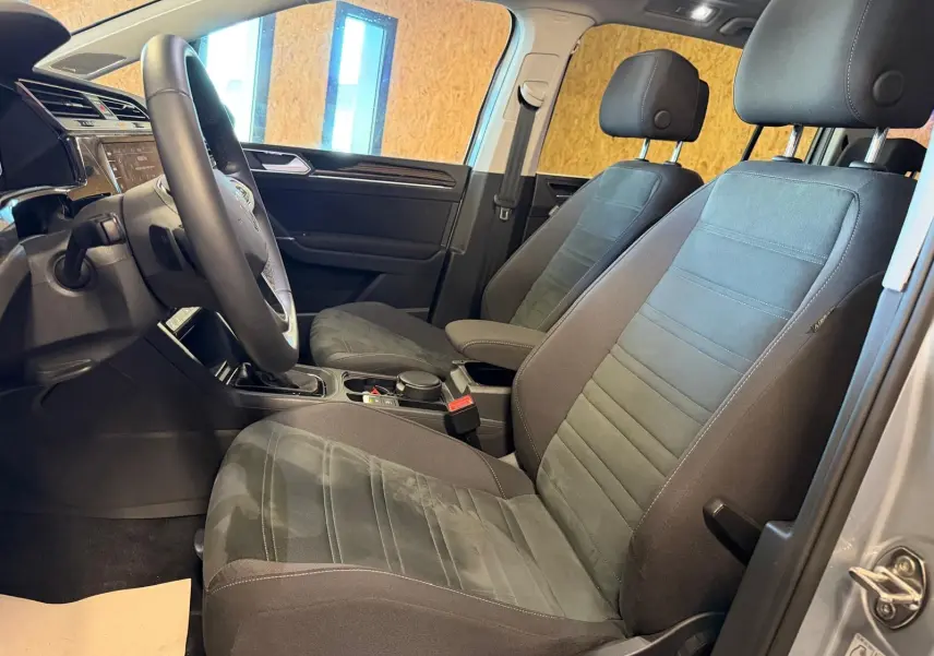 Vue intérieure côté conducteur du Volkswagen Touran gris 2025, montrant sièges avant et volant cuir multifonctions.