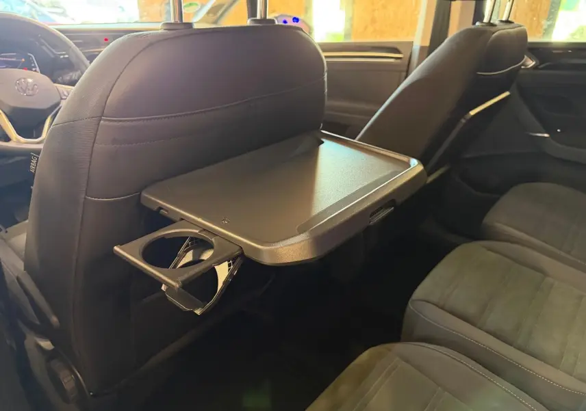 Vue intérieure du Volkswagen Touran 2.0 TDI gris, tablette pliable et porte-gobelet au dos du siège avant droit.
