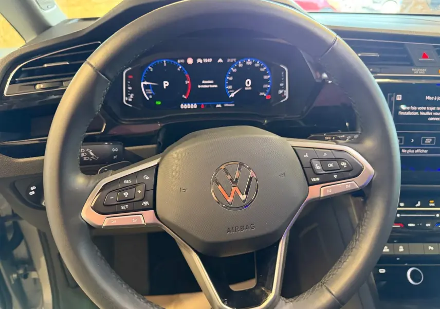 Vue rapprochée du volant cuir multifonctions noir du Volkswagen Touran 2025 avec tableau de bord digital et écran tactile.