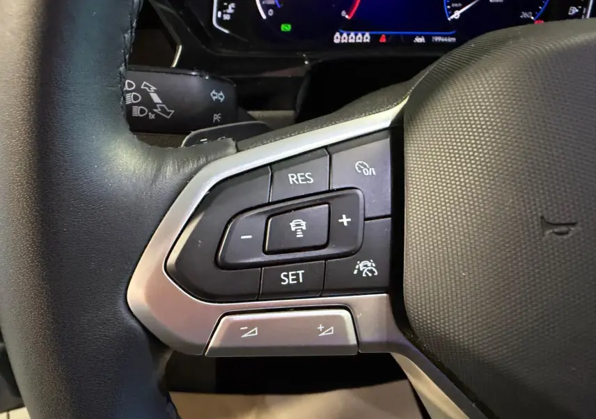 Gros plan sur les commandes du volant cuir noir du Volkswagen Touran 2025, avec régulateur de vitesse et aides à la conduite.