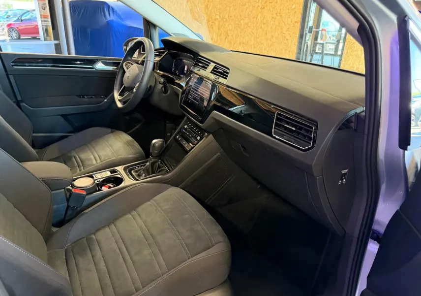 Vue intérieure côté conducteur du Volkswagen Touran gris 2025, mettant en valeur le tableau de bord et la console centrale moderne.