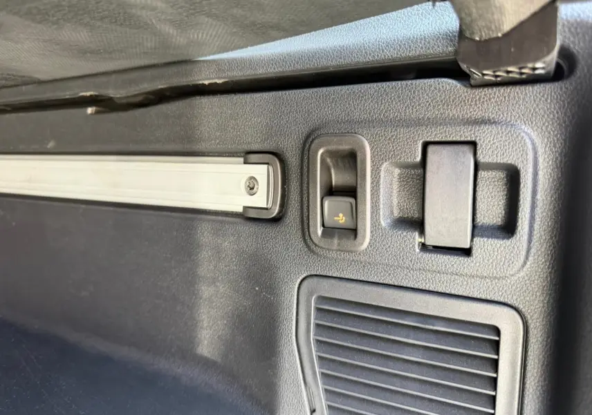 Détail intérieur du coffre du Volkswagen Touran gris, montrant un bouton de rabattement des sièges et une grille d'aération.