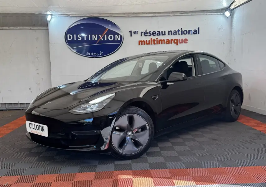 Tesla Model 3 Grande Autonomie noir, vue 3/4 avant droit dans un showroom avec sol à damiers rouge et noir.