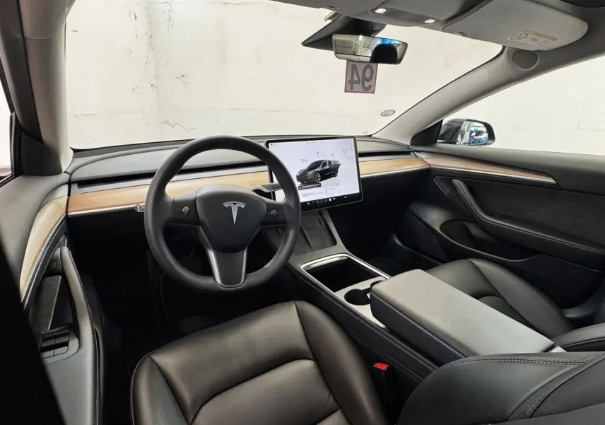 Intérieur Tesla Model 3 noir vue côté conducteur, tableau de bord épuré avec grand écran tactile central.