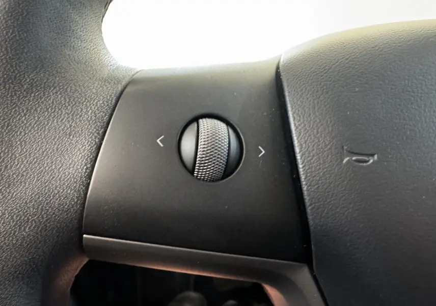 Gros plan sur la molette de réglage multifonctions du volant en cuir noir d'une Tesla Model 3 Grande Autonomie 2023.