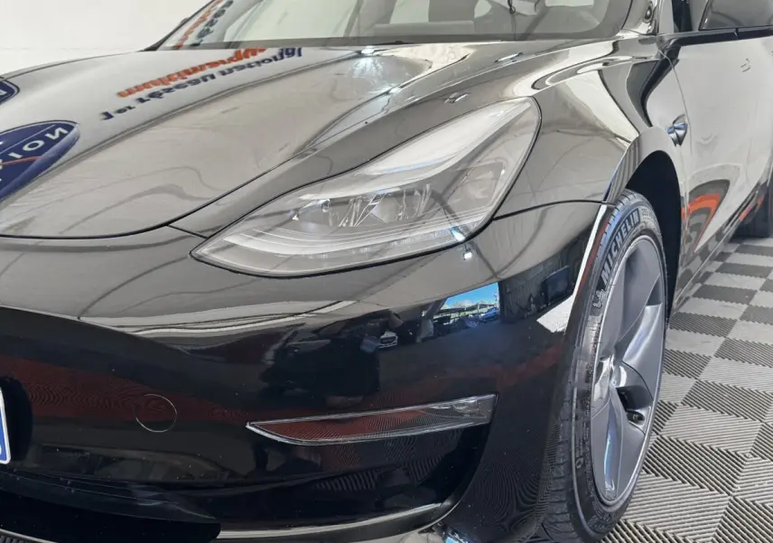 Vue 3/4 avant droit d'une Tesla Model 3 Grande Autonomie noire, mettant en valeur le phare et la roue Michelin.