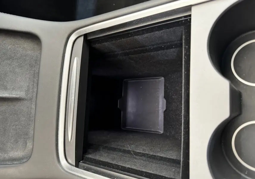 Vue rapprochée de la console centrale noire de la Tesla Model 3 2023, avec compartiment de rangement ouvert et porte-gobelets.