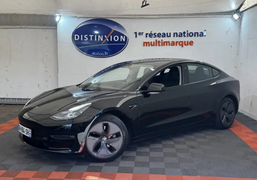 Tesla Model 3 Grande Autonomie noire vue 3/4 avant droit dans un showroom avec sol gris et orange.