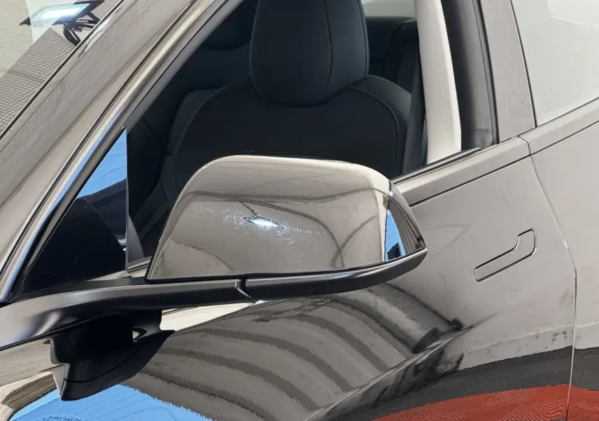 Gros plan sur le rétroviseur droit noir brillant d'une Tesla Model 3 Grande Autonomie 2023, avec porte et siège visibles.