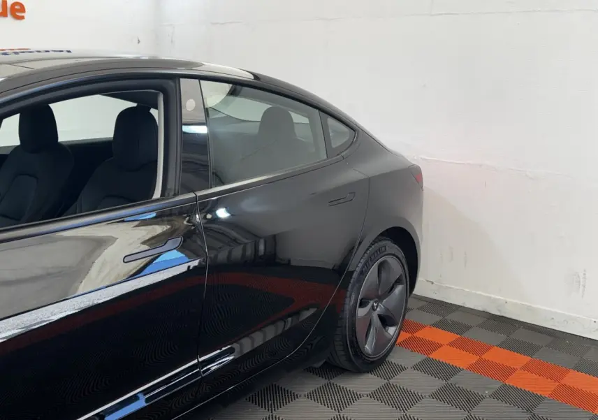 Vue côté gauche arrière d'une Tesla Model 3 Grande Autonomie noire, avec jante aérodynamique et poignée affleurante.