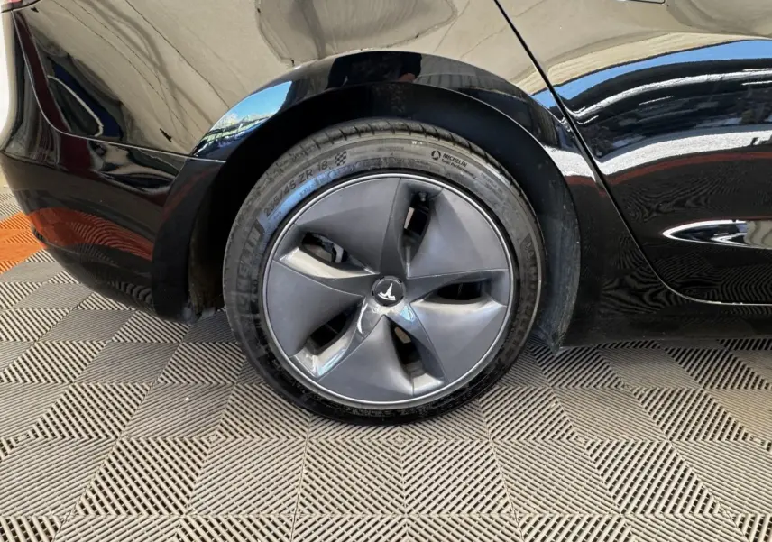 Gros plan sur la roue arrière droite noire d'une Tesla Model 3 Grande Autonomie 2023 avec jante aérodynamique.