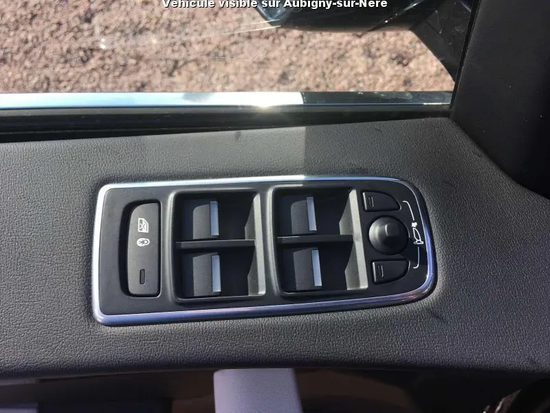Gros plan sur les commandes des vitres électriques et rétroviseurs sur la porte intérieure côté conducteur d'une Jaguar F-PACE noire.