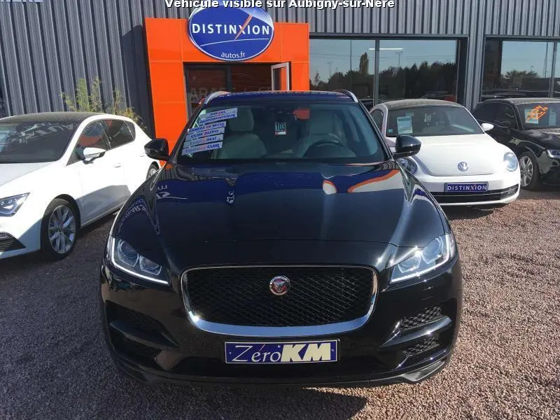 Vue frontale d'un Jaguar F-PACE noir métallisé, avec calandre chromée et phares LED allumés, sur un parking extérieur.