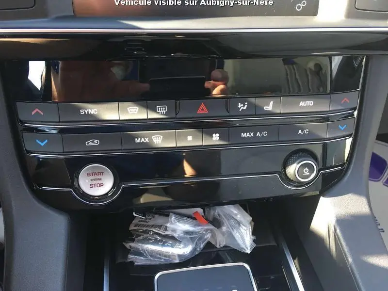 Vue rapprochée du tableau de bord noir brillant du Jaguar F-PACE 2018, avec commandes climatisation et bouton start/stop visibles.