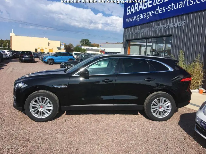 Jaguar F-PACE noir vue de profil côté gauche, avec jantes argentées et vitres surteintées, stationné devant un garage.