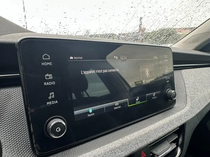 Écran tactile multimédia du tableau de bord de la Skoda Scala blanc cristal, vue de côté droit sous la pluie.