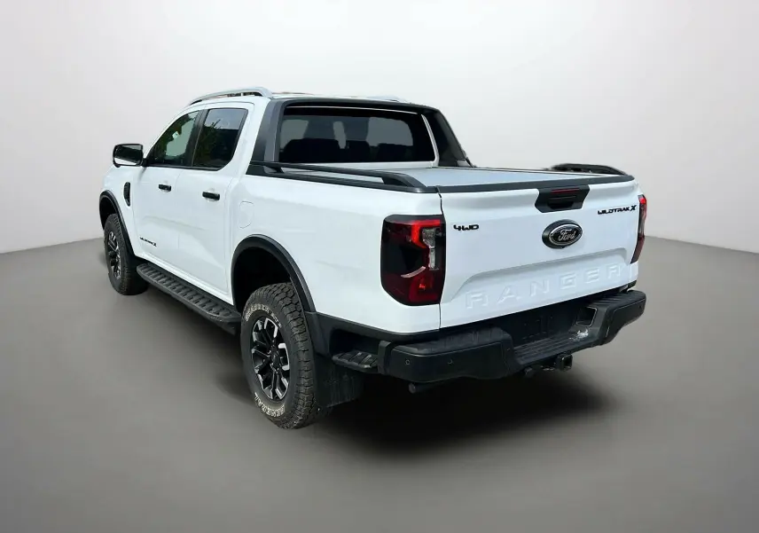 Vue 3/4 arrière droite du Ford Ranger Wildtrak X blanc glacier avec barres de toit et jantes noires.