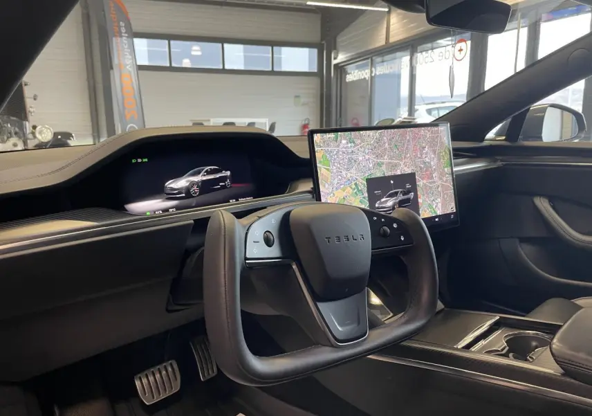 Vue intérieure côté conducteur du Tesla Model S Plaid 2023 avec volant carré et écran tactile central affichant une carte.