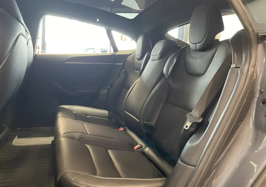 Vue intérieure côté droit des sièges arrière noirs en cuir d'une Tesla Model S Plaid 2023 gris foncé avec ceintures de sécurité visibles.