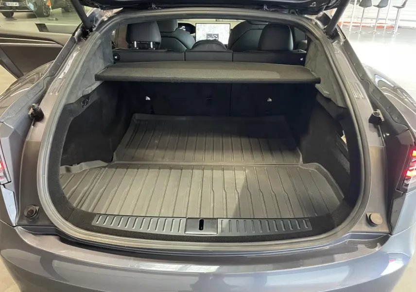 Coffre ouvert vu de l'arrière d'une Tesla Model S Plaid gris foncé avec cache-bagages et intérieur noir.