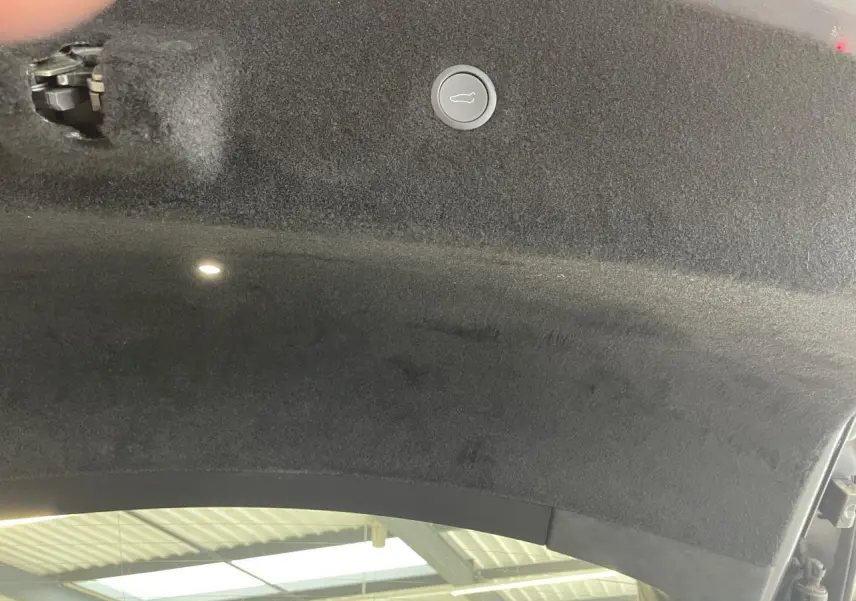 Détail intérieur du coffre ouvert d'une Tesla Model S Plaid gris foncé, montrant la garniture et le bouton de fermeture.
