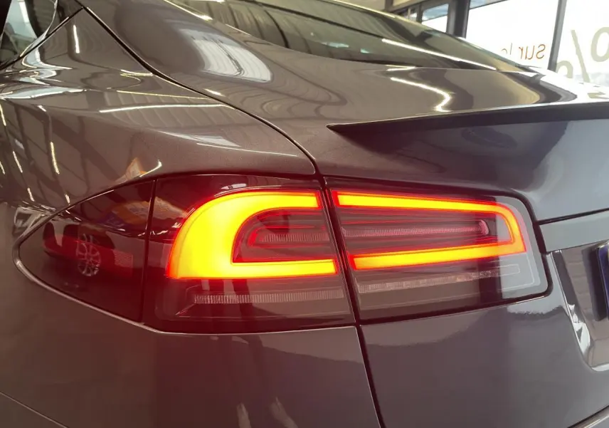 Gros plan sur le feu arrière droit allumé d’une Tesla Model S Plaid gris foncé, soulignant la finition métallique.