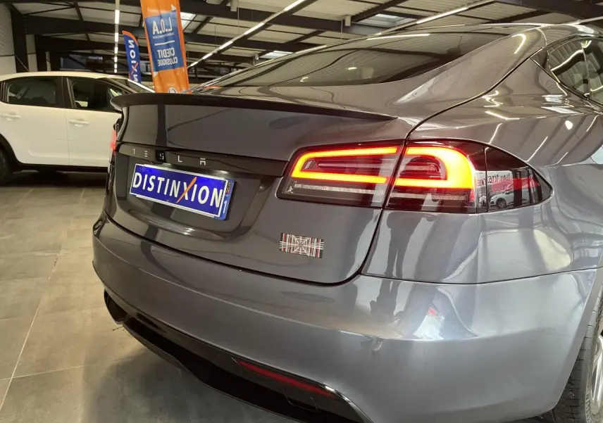 Vue 3/4 arrière droite d'une Tesla Model S Plaid gris foncé avec feux arrière LED allumés en showroom.