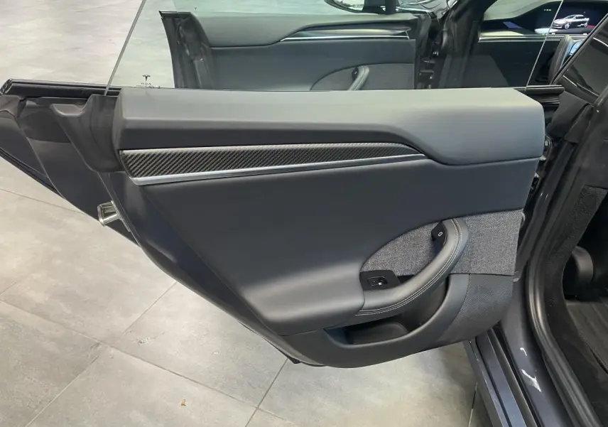 Vue intérieure de la porte arrière gauche gris foncé d'une Tesla Model S Plaid 2023 avec insert carbone et tissu gris.