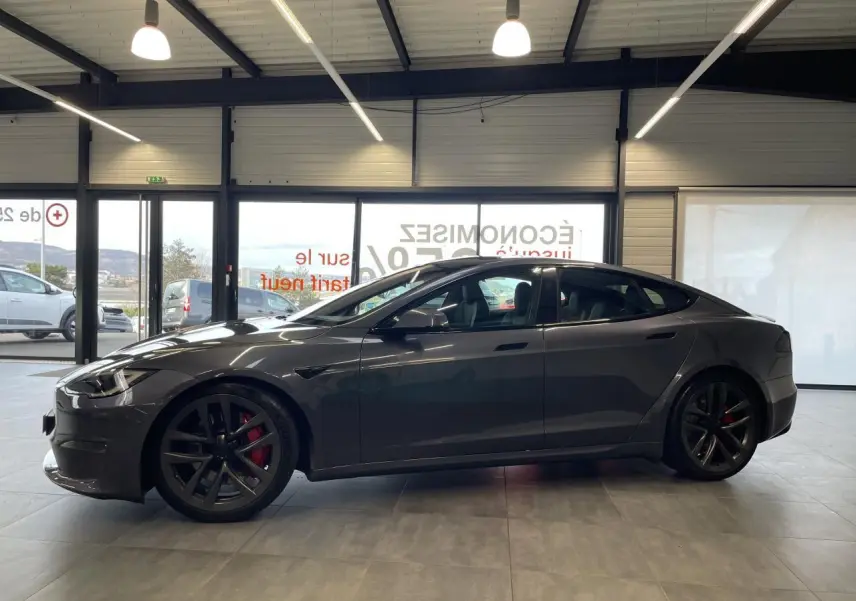 Tesla Model S Plaid gris foncé vue de profil côté gauche, jantes noires avec étriers de frein rouges, intérieur visible.