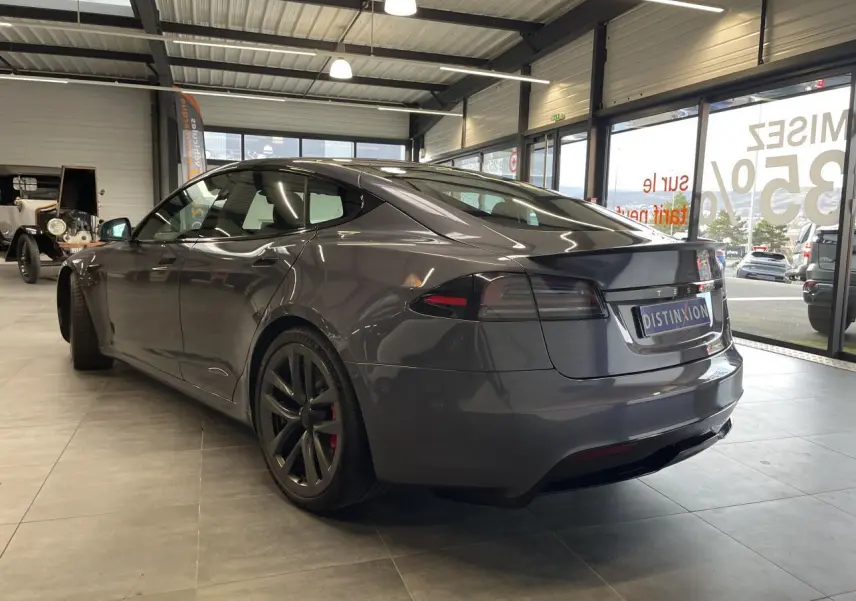Tesla Model S Plaid gris foncé vue 3/4 arrière droit en intérieur avec jantes noires et spoiler arrière.