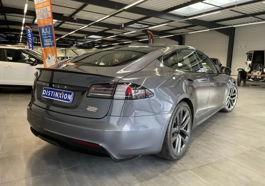 Tesla Model S Plaid gris foncé vue 3/4 arrière droit en intérieur avec jantes aluminium distinctives.