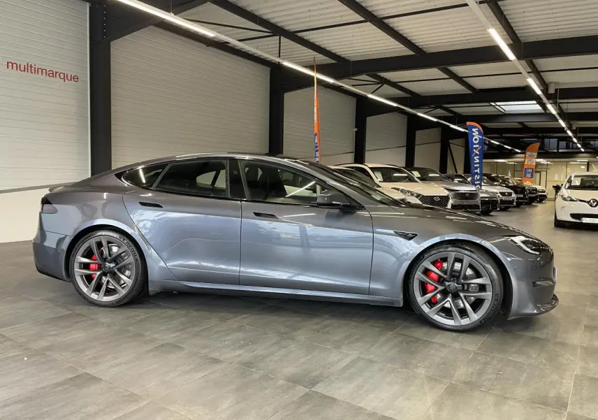 Tesla Model S Plaid gris foncé vue de profil côté gauche dans un showroom avec jantes sport et étriers rouges.