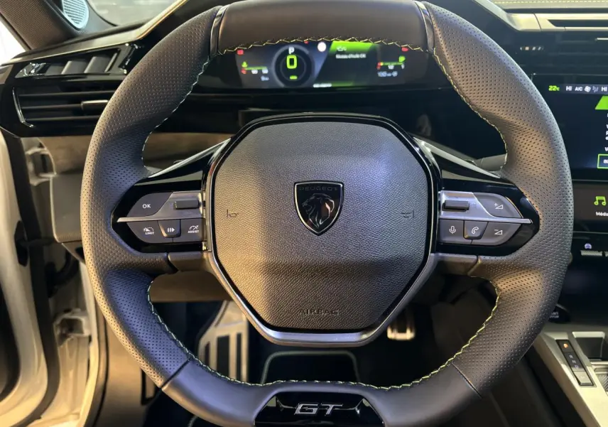 Gros plan sur le volant GT en cuir perforé avec surpiqûres vert Adamite de la Peugeot 308 hybride 2026.