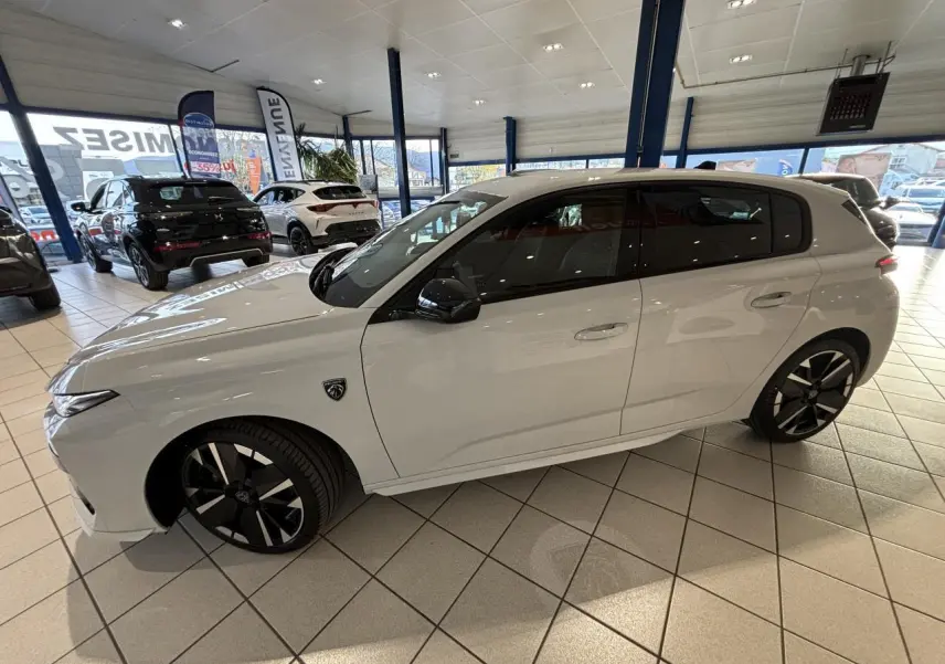Vue latérale droite d'une Peugeot 308 blanche Okenite avec jantes alliage bi-tons et rétroviseurs noirs brillants en showroom.
