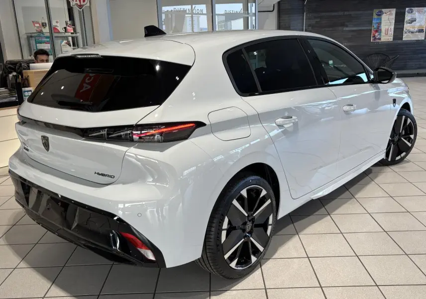 Vue 3/4 arrière droite d'une Peugeot 308 hybride blanche Okenite avec jantes alliage bicolores et vitres teintées.