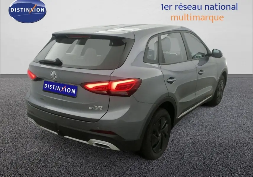 Vue 3/4 arrière droite du SUV MG ZS hybride gris Hampstead avec feux arrière allumés sur fond neutre.
