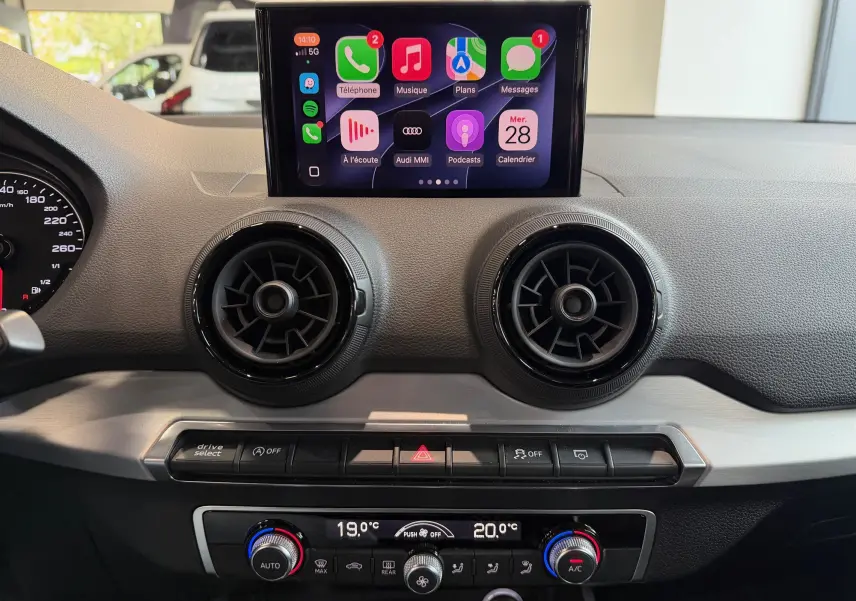 Vue intérieure du tableau de bord de l'Audi Q2 gris, avec écran tactile central affichant Apple CarPlay et aérateurs ronds noirs.