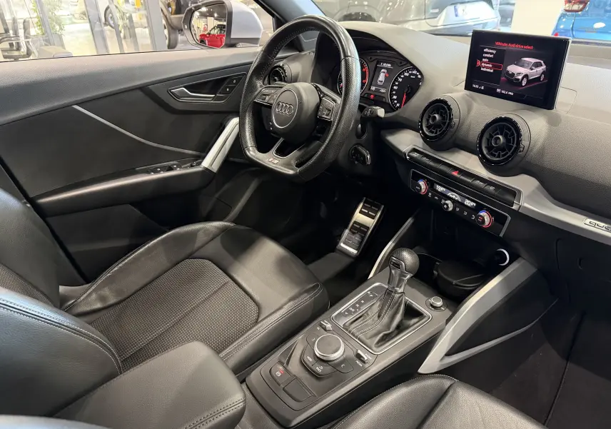 Vue intérieure côté conducteur de l'Audi Q2 2017, avec volant cuir, tableau de bord digital et console centrale moderne.