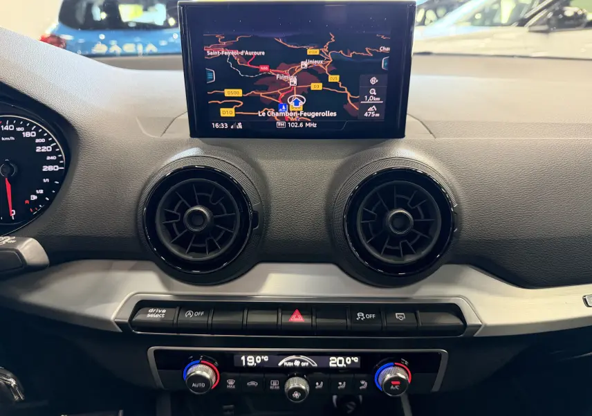 Vue intérieure du tableau de bord de l'Audi Q2 2017 avec écran GPS, aérateurs ronds noirs et commandes de climatisation.