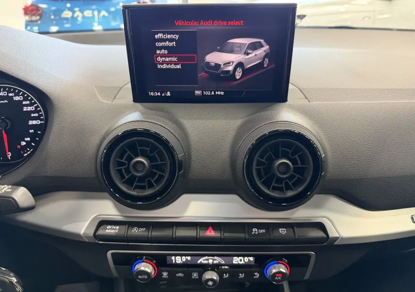Vue intérieure du tableau de bord de l'Audi Q2 gris, avec écran central affichant le mode de conduite dynamic.