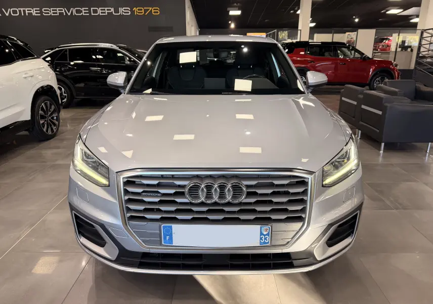 Audi Q2 gris vue de face en intérieur, avec calandre hexagonale et feux LED allumés.