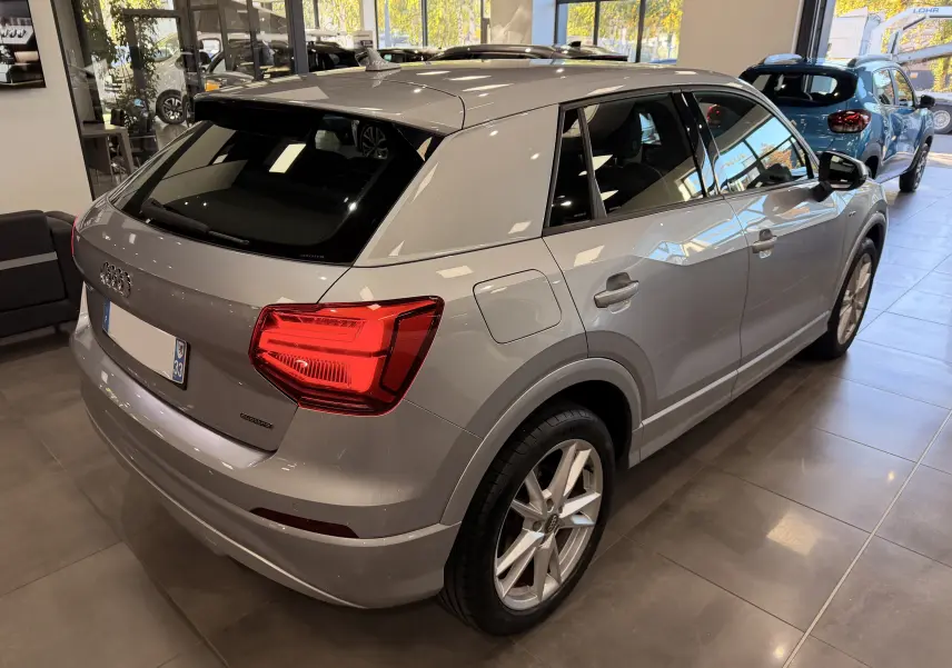 Audi Q2 gris vue 3/4 arrière droit en intérieur, avec feux arrière allumés et jantes alliage visibles.