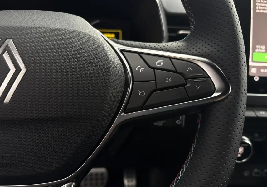 Gros plan sur le côté droit du volant perforé de la Renault Clio 2025 avec commandes multifonctions et surpiqûres bleues.