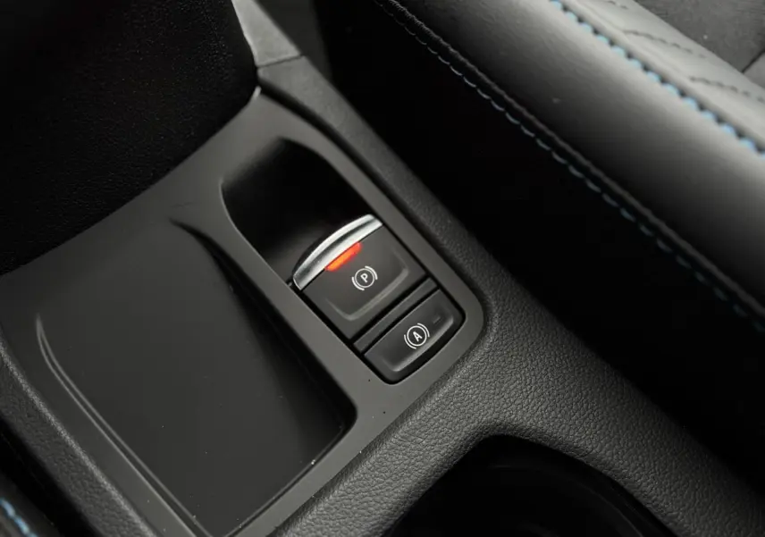 Gros plan sur la console centrale noire avec bouton frein à main électronique allumé et surpiqûres bleues Renault Clio 2025