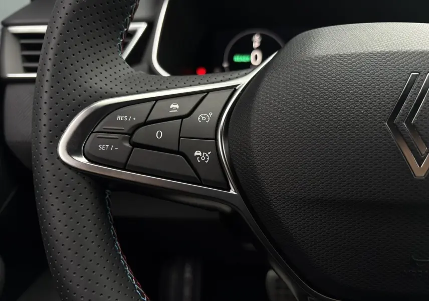 Gros plan sur le volant perforé noir avec surpiqûres bleues de la Renault Clio V NV E-Tech 2025, boutons multifonctions visibles.