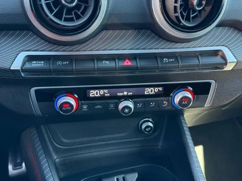 Vue rapprochée de la console centrale de l'Audi Q2 35 TDI 150ch S line 2025, avec commandes climatisation et design en gris nacré.