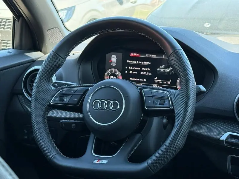 Vue intérieure centrée sur le volant perforé de l'Audi Q2 35 TDI S line 2025 avec tableau de bord numérique allumé.