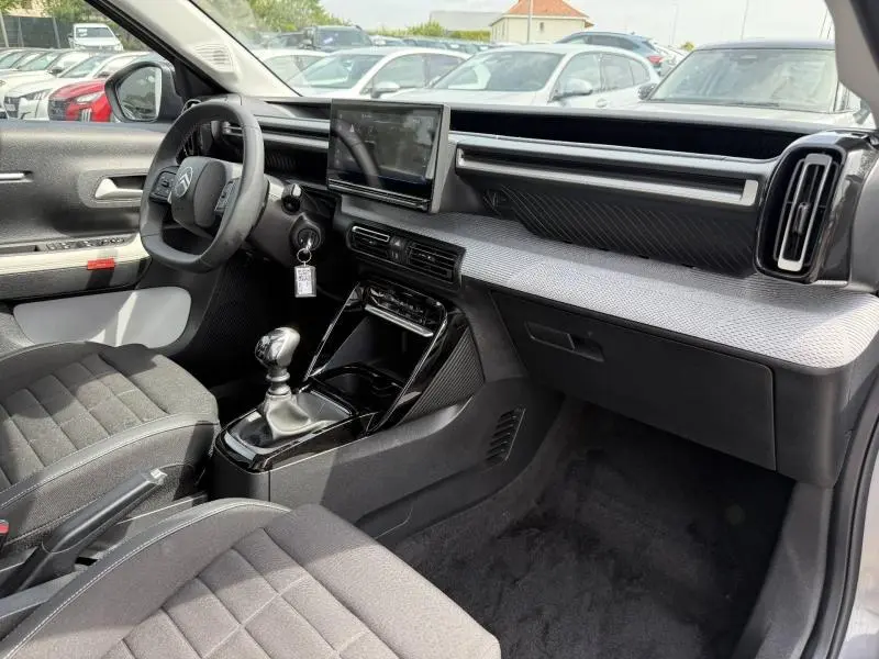 Vue intérieure côté conducteur de la Citroën C3 1.2 Turbo 2025 avec tableau de bord gris et écran tactile central.