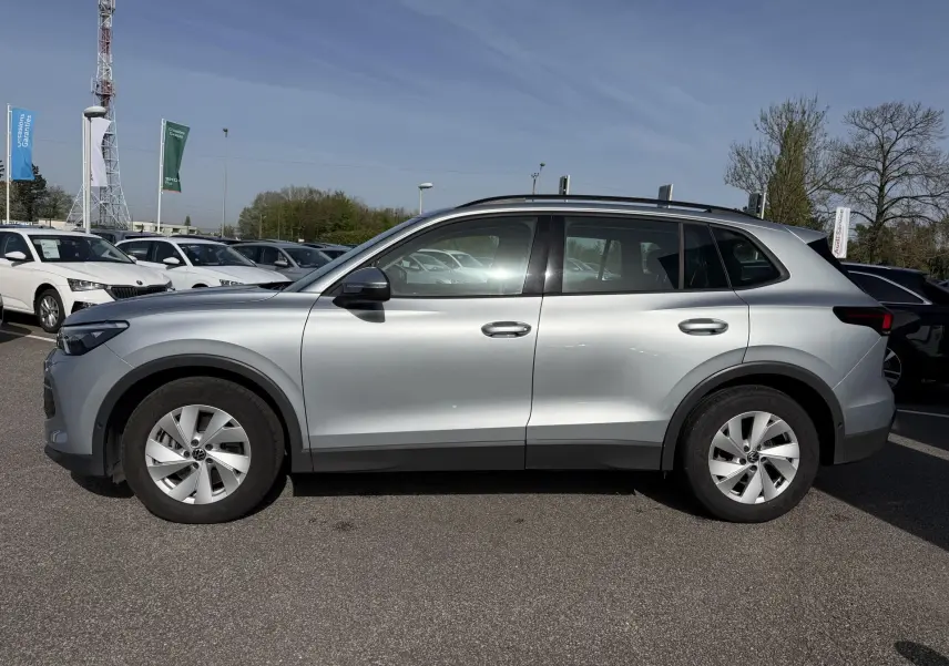 Profil droit d’un Volkswagen Tiguan gris 2025, avec jantes alliage 17 pouces et barres de toit noires.