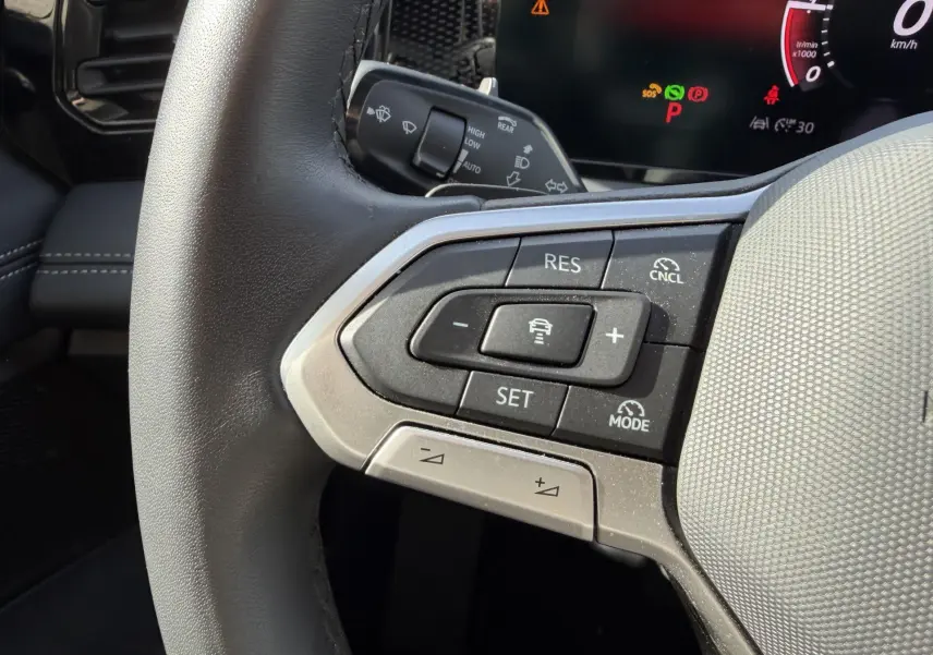 Gros plan sur les commandes multifonctions côté gauche du volant cuir du Volkswagen Tiguan 2025 avec affichage digital en arrière-plan.